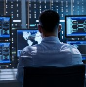 System Security Specialist Working at System Control Center. Room is Full of Screens Displaying Various Information.